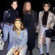 Cindy Crawford 1991 wears a leather blazer and blue jeans at LAX. Tyra Banks wears double denim and a baseball cap in 1993. Jennifer Aniston wears a long black coat, blue mini skirt, knee-high boots, and a black boatneck top. Halle Berry wears an animal print coat, black turtleneck, and blue jeans at LAX in 1994. 
