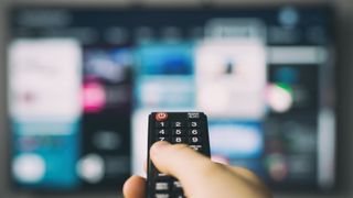 Hand holding up remote to blurred out TV screen in the background