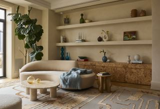 A neutral living room with a burl wood side table, open shelving, and a beige curved sofa