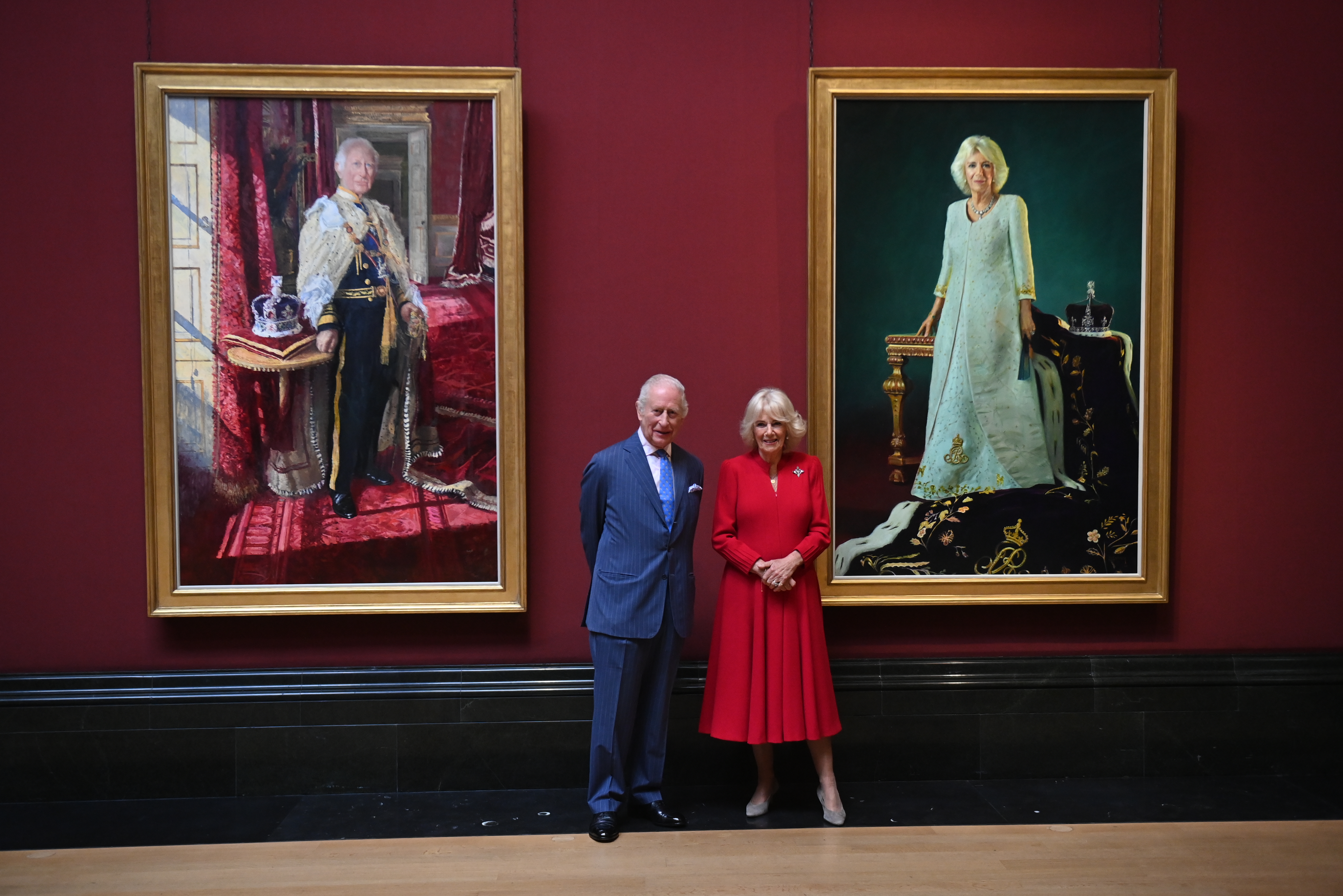 Queen Camilla and King Charles standing in front of their coronation portraits at Buckingham Palace