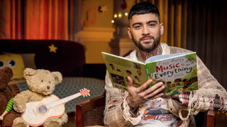 Former One Direction star Zayn Malik sits next to a teddy bear holding a toy guitar to read a "Bedtime Story" on CBeebies