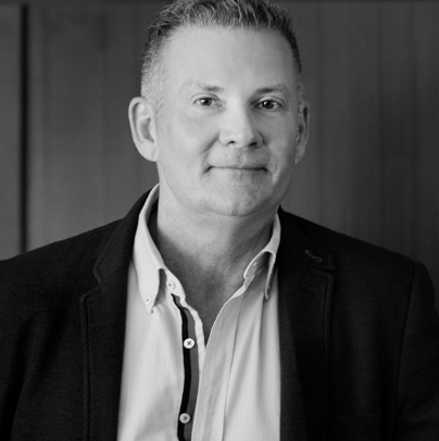 A black and white headshot of man in a shirt and jacket