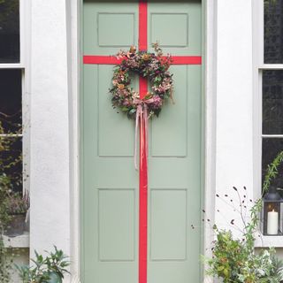 Sage green front door wrapped in red bow with Christmas wreath on top.