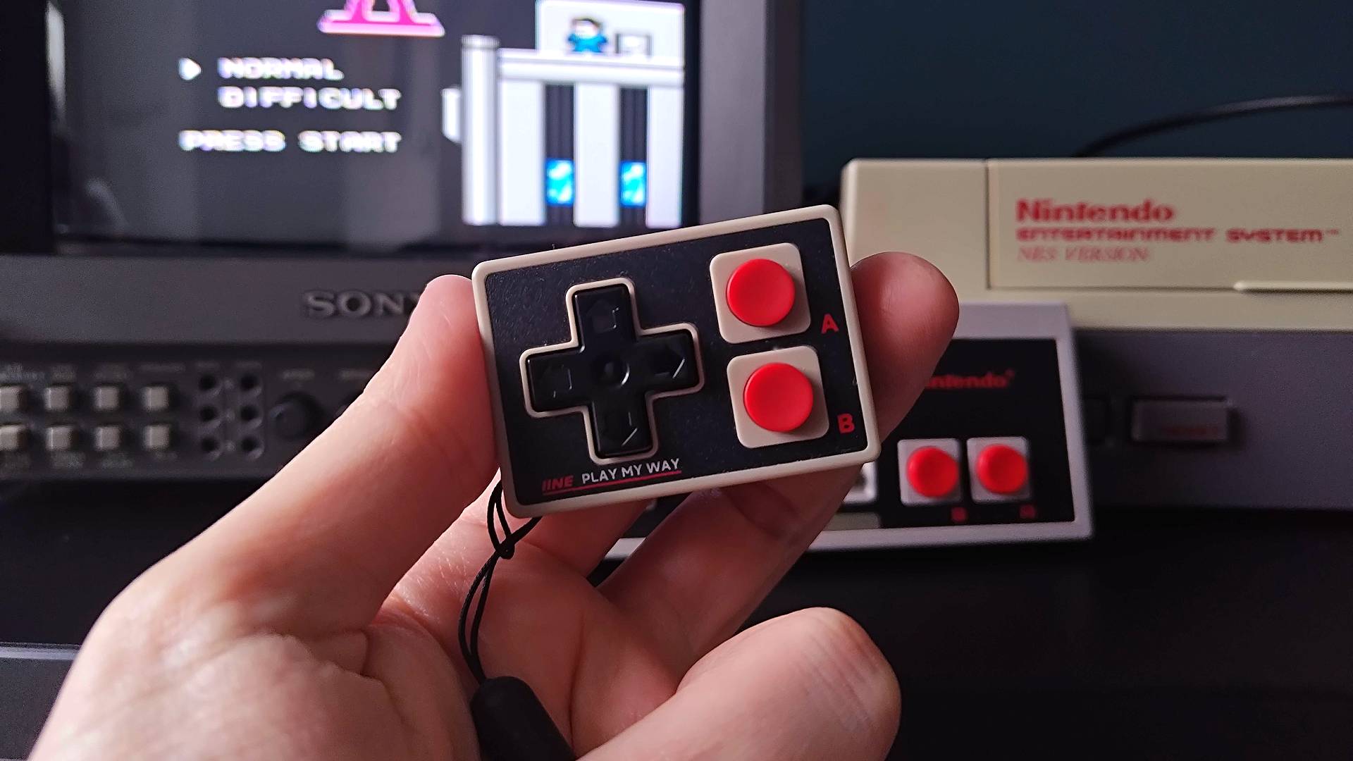 Hand holding IINE Gamebrick Mini controller with NES in backdrop next to Sony Trinitron PVM CRT and Mega Man 2 intro on screen.