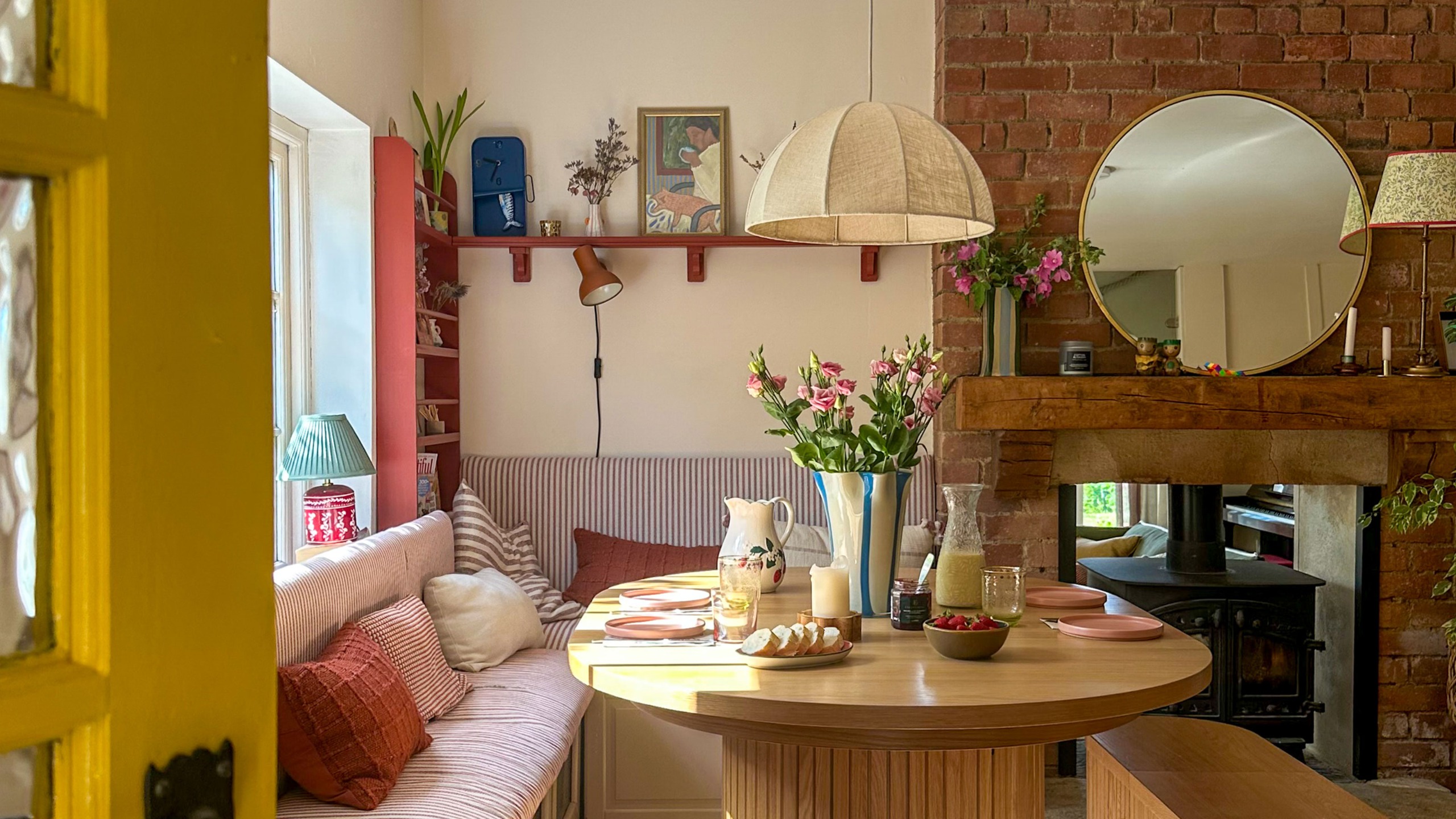 Kitchen dining area with red and white striped upholstered banqeuette around wooden table topped with pendant lampshade