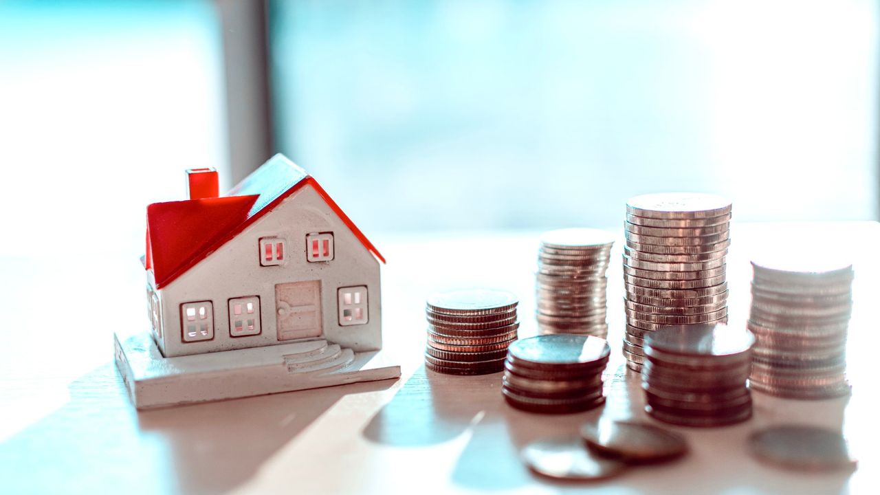 Model of a house next to piles of coins