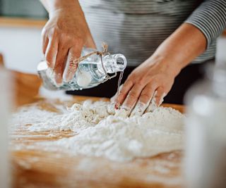 Woman pouring water on wheat flour on the table