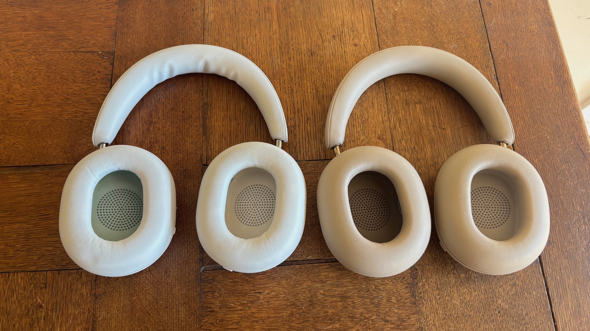 The Sonos Ace Ultra and Sonos Ace headphones laid side by side on a wooden surface with their earcups turned to show their insides.
