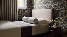 a bedroom with a decorative neutral wall paper, and a bed with circular pillows on