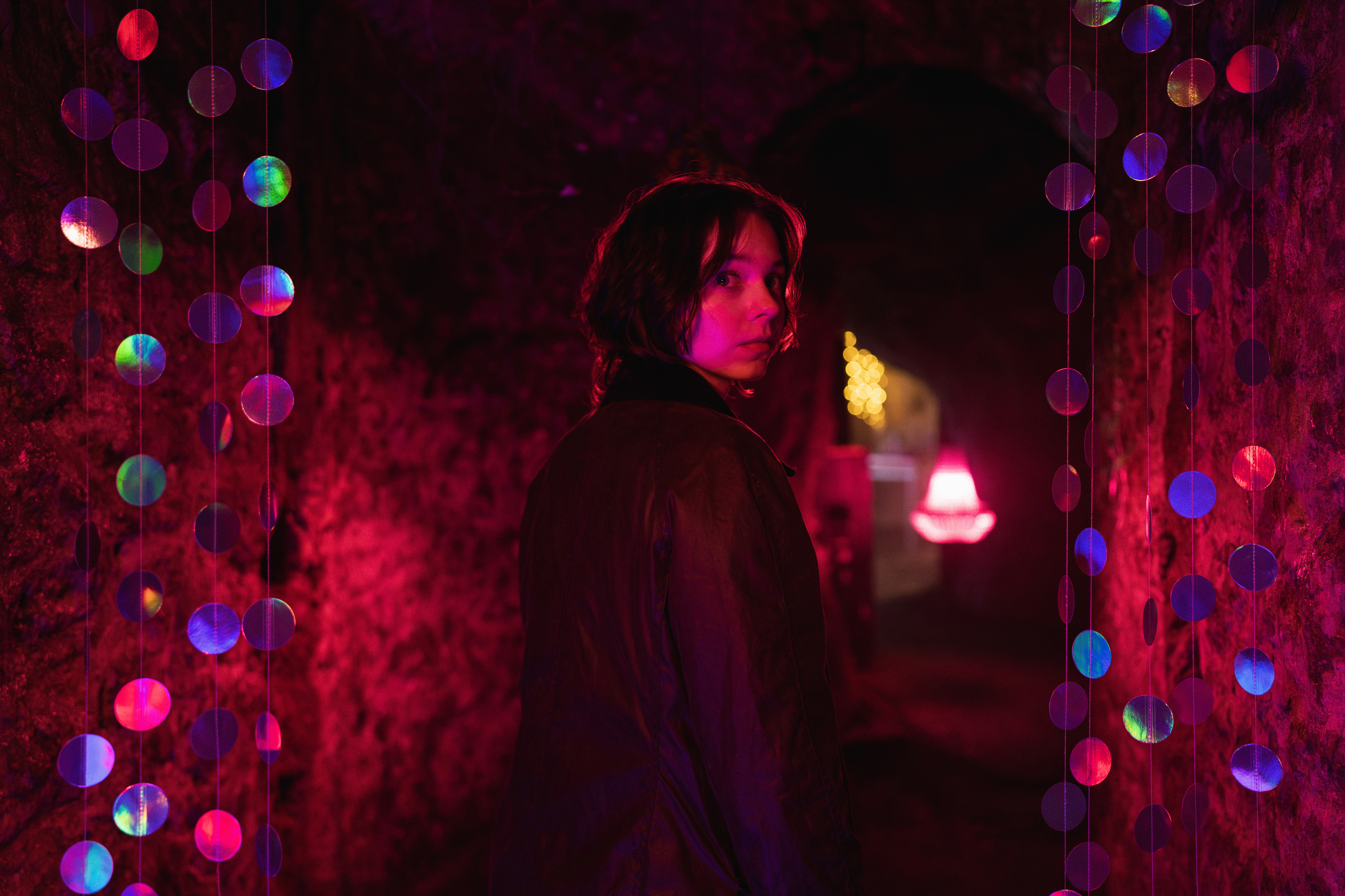 Emma Myers as Pip Fitz-Amobi walking down a red lit hallway through a sparkly curtain in A Good Girl's Guide to Murder: Season 2