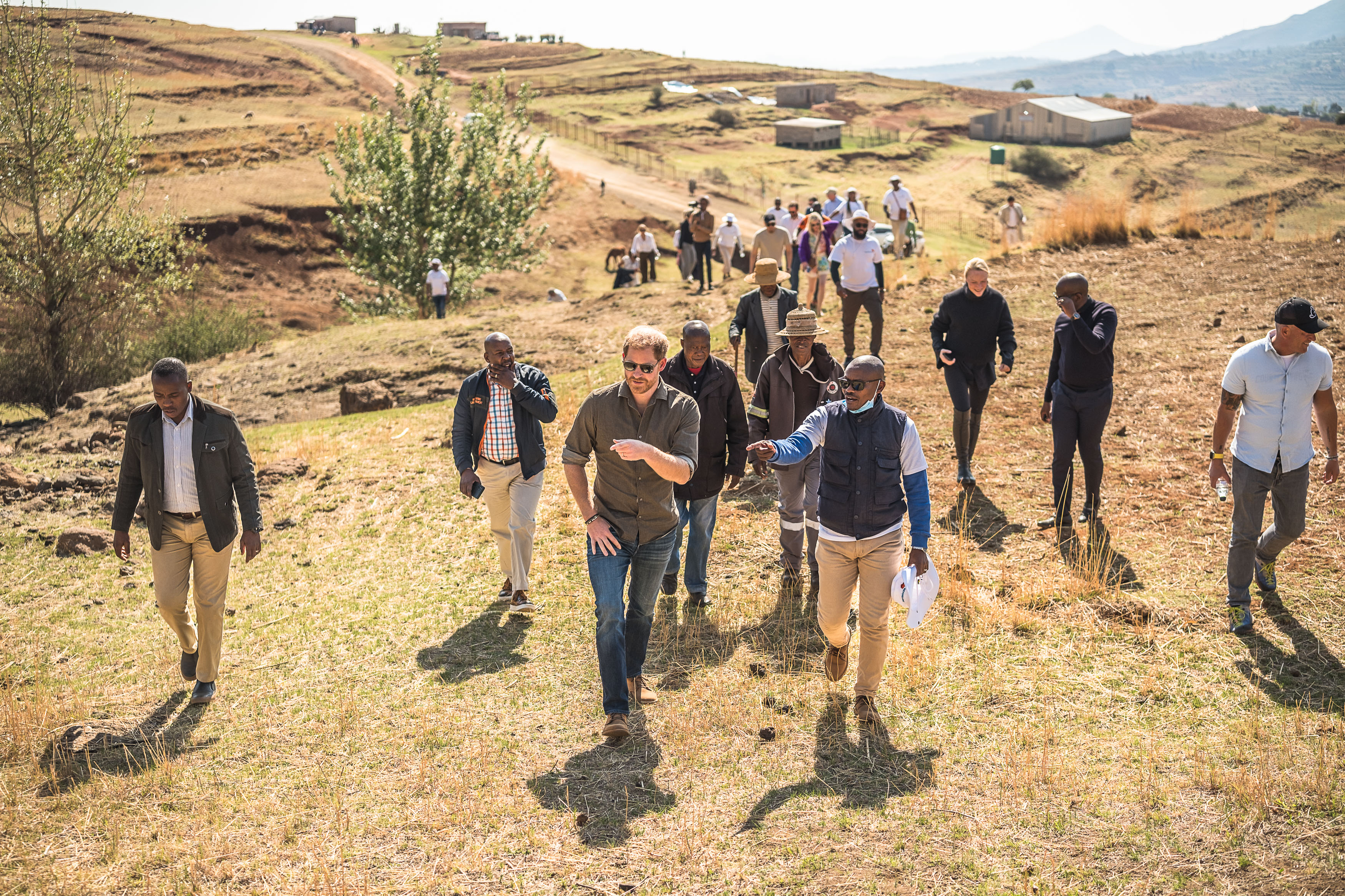 Prince Harry walking across a hill with a crowd of people in Lesotho
