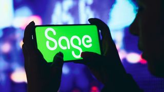 A silhouetted woman holds a smartphone with the Sage Group logo displayed on the screen