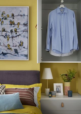 bedroom with yellow wall and shirts hanging in wardrobe