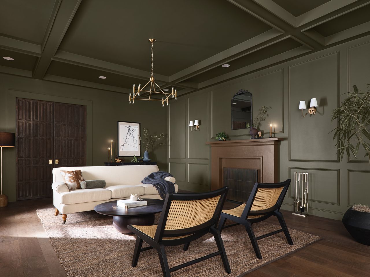 A living room with dark green walls, a cream sofa, and bamboo cane chairs