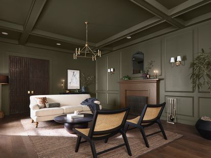 A living room with dark green walls, a cream sofa, and bamboo cane chairs