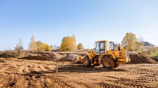 A yellow digger flattening soil on a building plot