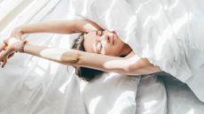 Woman sleeping happily in the heat, stretching arms above duvet