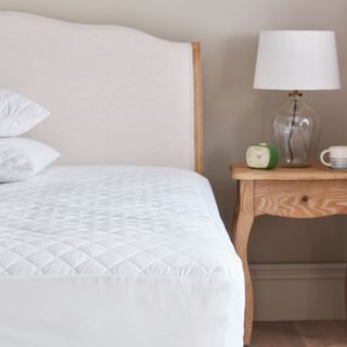 A mattress protector on a bed with a wood and cream upholstered headboard