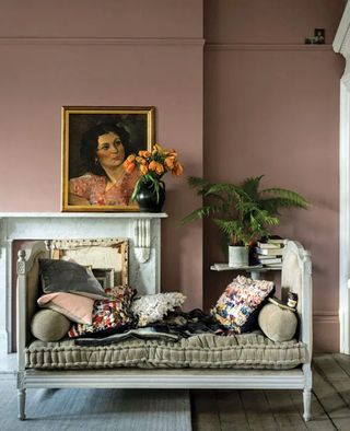 Living room paint ideas in Sulking Room Pink by Farrow & Ball, with a gilt framed oil painting propped onto a stone fireplace and a vintage white painted day bed.