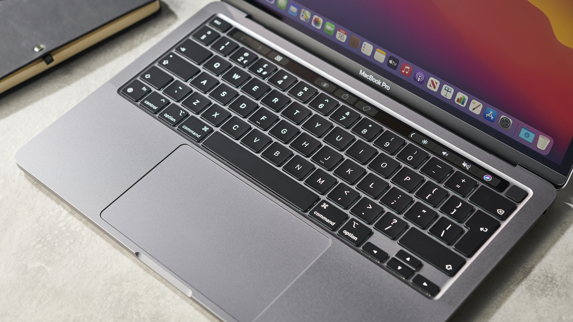 Apple MacBook Pro 13-inch (M1, 2020) on a marble surface next to a notebook and a pen