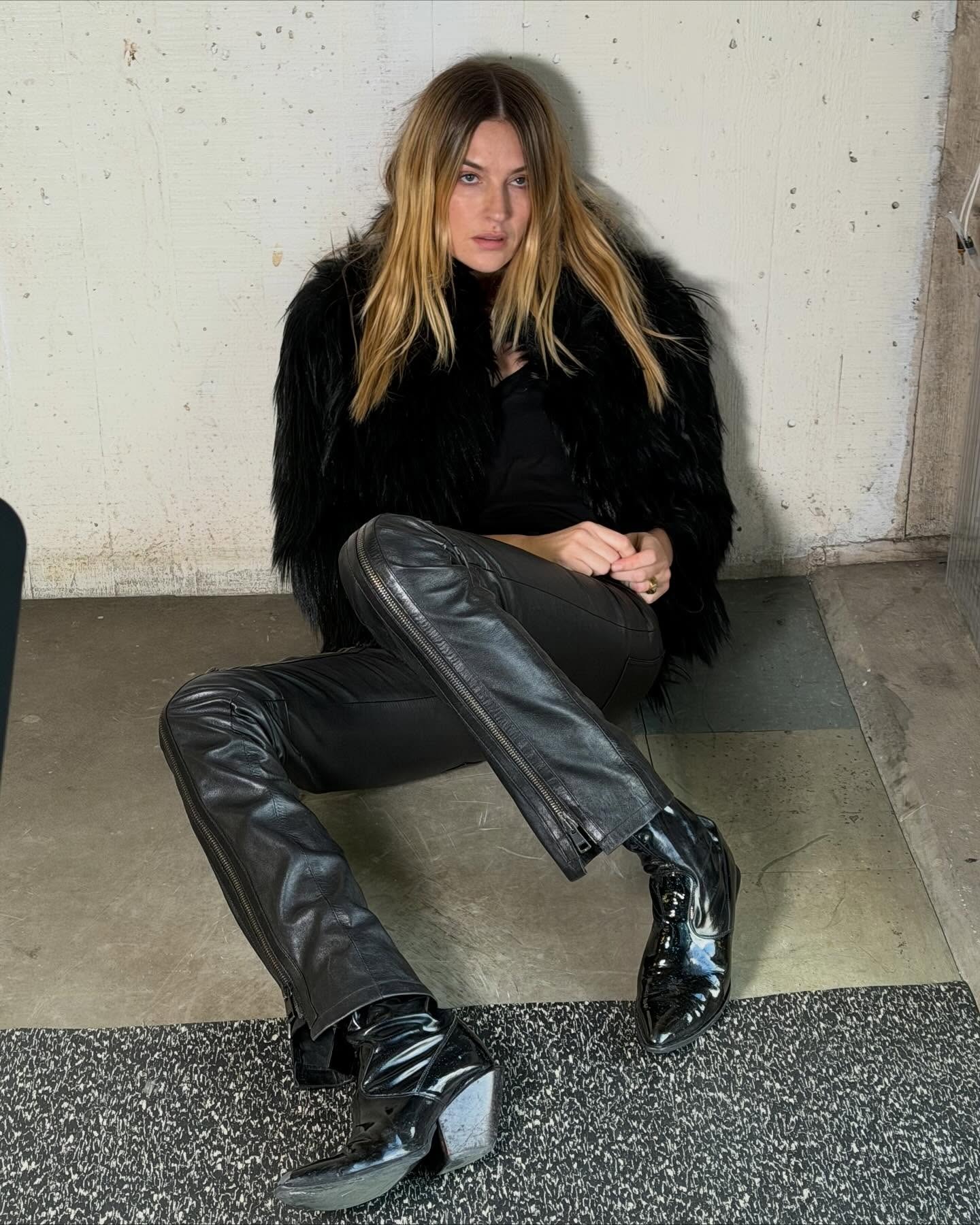 Influencer @camillecharriere wears a black fur jacket with black leather trousers and black patent leather boots.