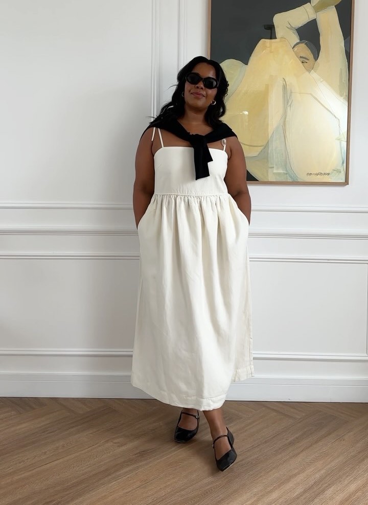 Karina in a white dress with a black jumper tied around her shoulders