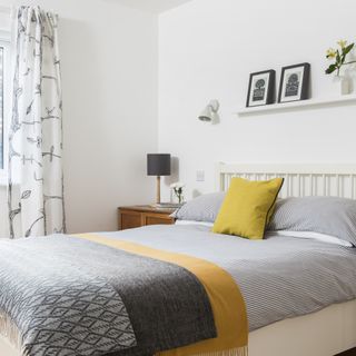 white bedroom with patterned curtains, picture rail above bed and wall light