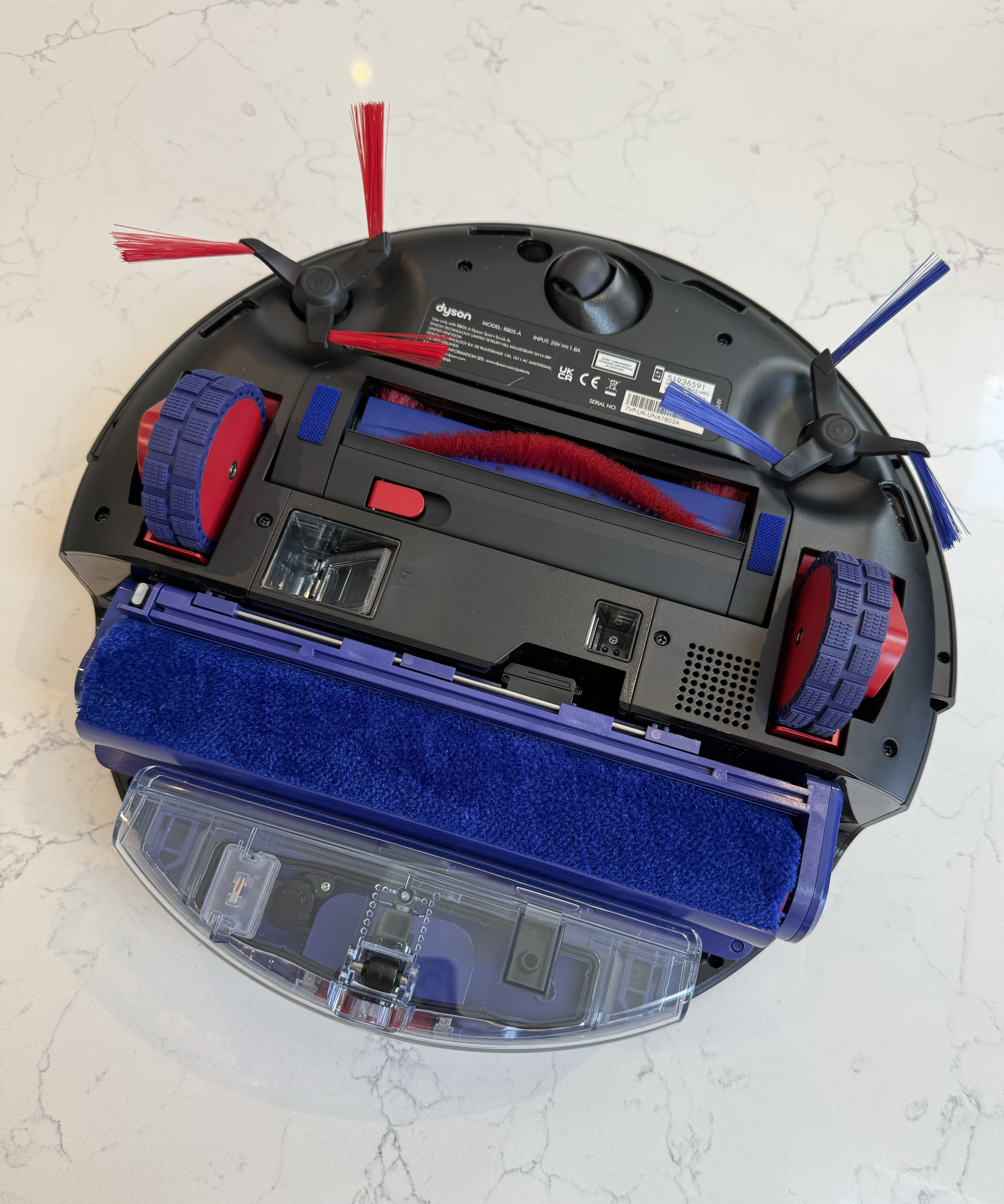 Overhead underside view of the Dyson Spot+Scrub Ai showing side brushes, drive wheels, brush bar and wet roller