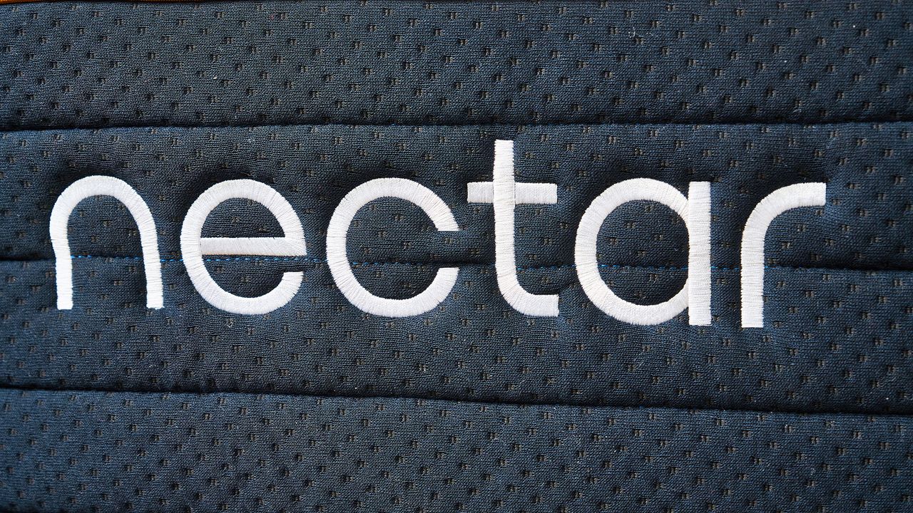 A close up of the white Nectar logo embroidered onto the side of the Nectar Ultra Hybrid dark blue base cover