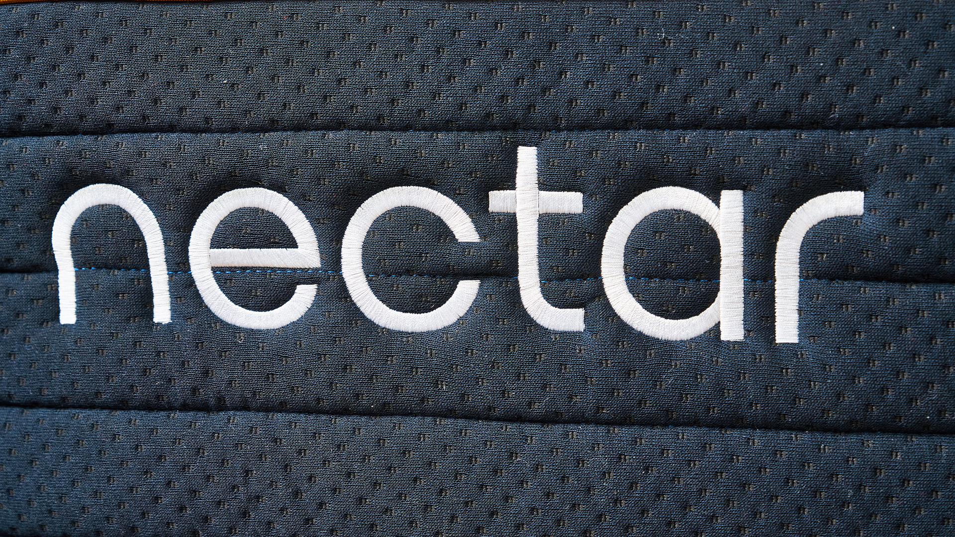 A close up of the white Nectar logo embroidered onto the side of the Nectar Ultra Hybrid dark blue base cover