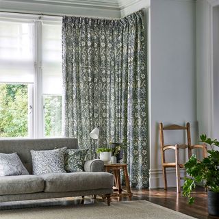 living room with grey walls, wooden floor, green pattern curtains and a grey sofa with pattern cushions