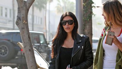 Kim Kardashian wearing all black and sunglasses, walking in the street