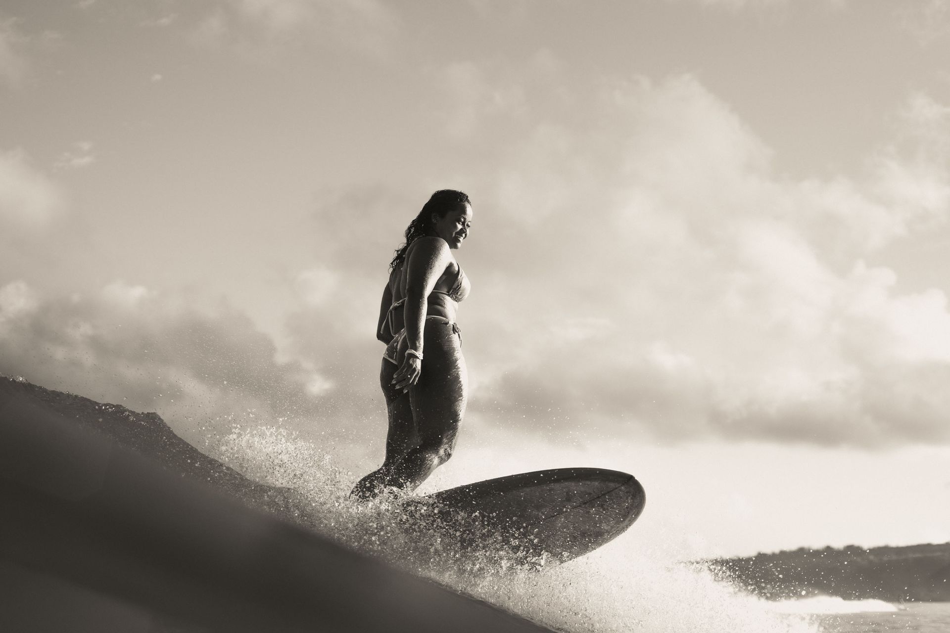 The atmospheric image shows pro-surfer Suelen Naraisa standing ontop of her surfboard mid surf.
