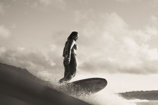 The atmospheric image shows pro-surfer Suelen Naraisa standing ontop of her surfboard mid surf.