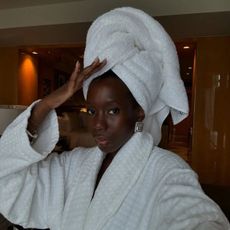 A woman with glowing skin wearing a white hotel robe and a white towel on her head