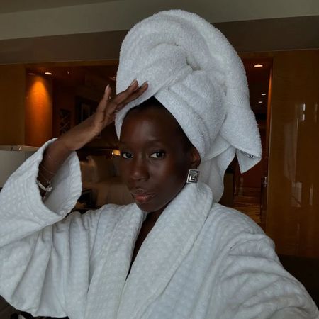 A woman with glowing skin wearing a white hotel robe and a white towel on her head