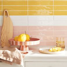 A pink striped lemon dish sat against a glossy wall tiled in pink white and yellow