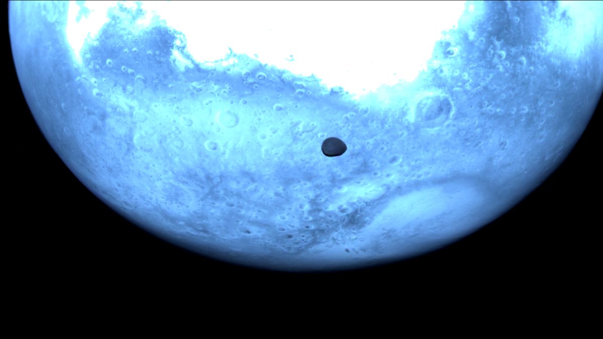 a small moon is silhouetted against a planet in the light blue hue of near-infrared