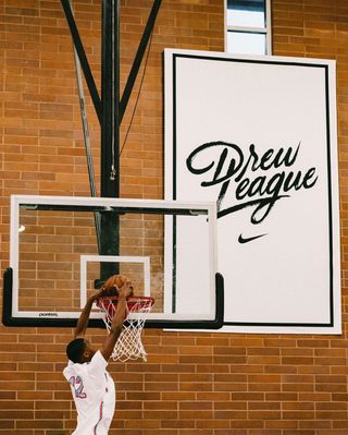Man dunks basketball into net next to the Drew League logo