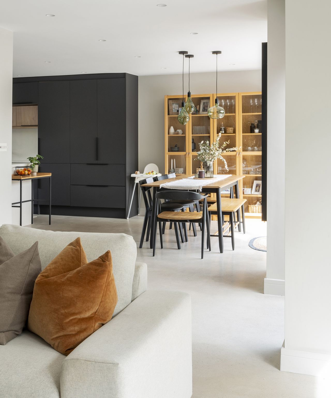 An open plan kitchen/diner/lounge in a contemporary house extension. There is a plush pale sofa with cushions in the foreground and a family dining table in front of dark wood kitchen cabinets in the background