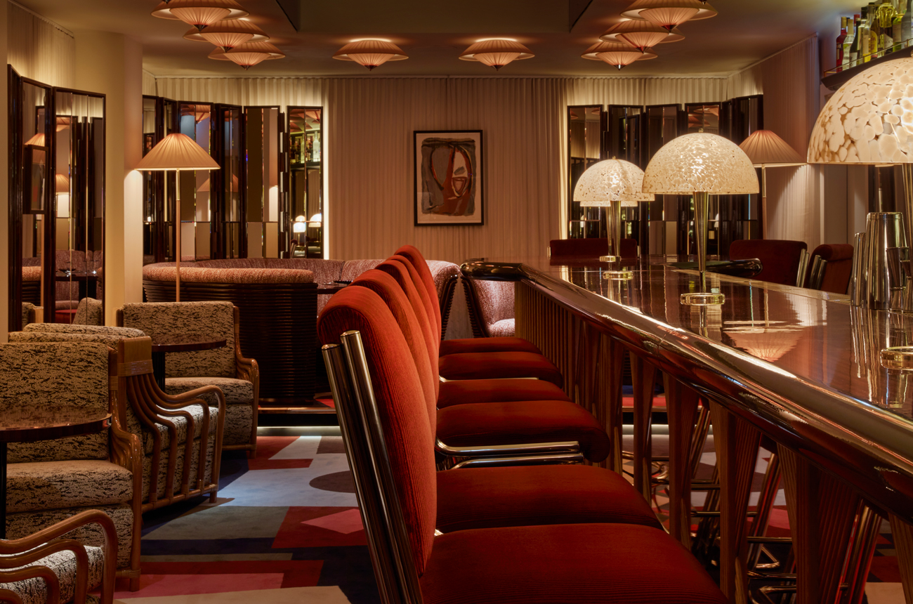 A lounge bar with red velvet bar stools and lamps