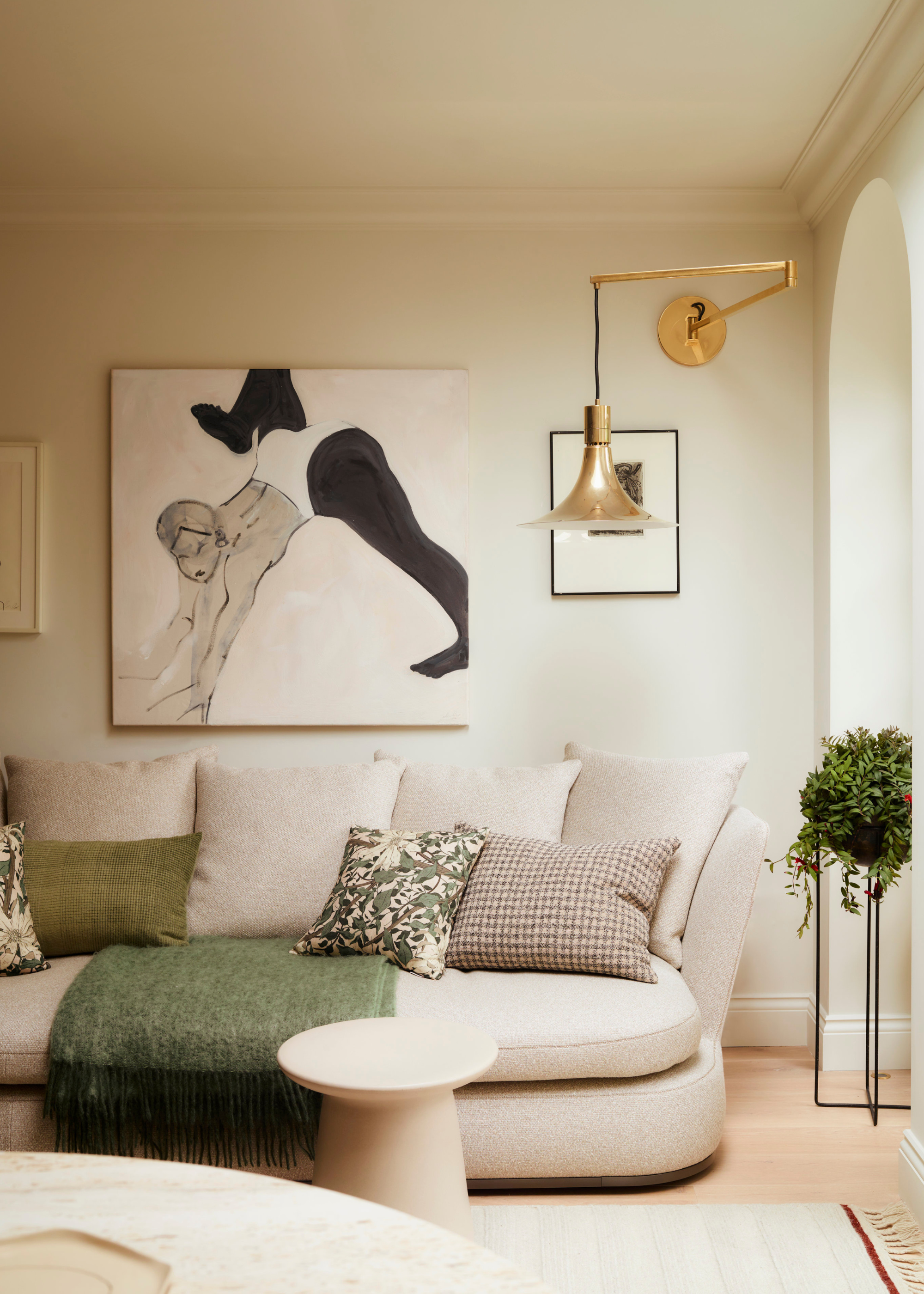 A living room with wall art, a bronze pendant sconce, a sofa with pillows, a potted trailing plant, and a side table