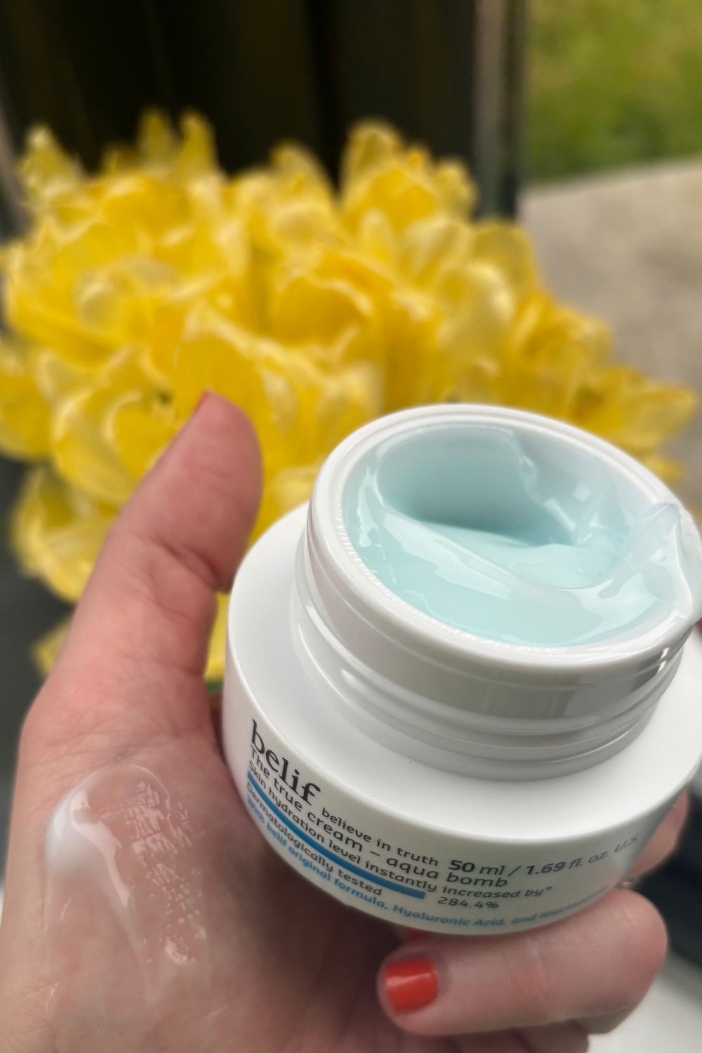 a hand holding a tub of belif aqua bomb cream