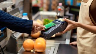Cropped view of young adult man holding plastic credit card in hand, using terminal and paying for shopping in supermarket