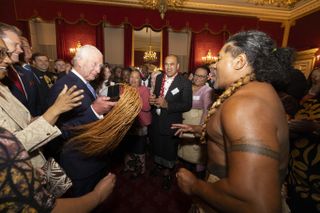 King Charles waving a tassel and dancing with a Samoan rugby player at Buckingham Palace