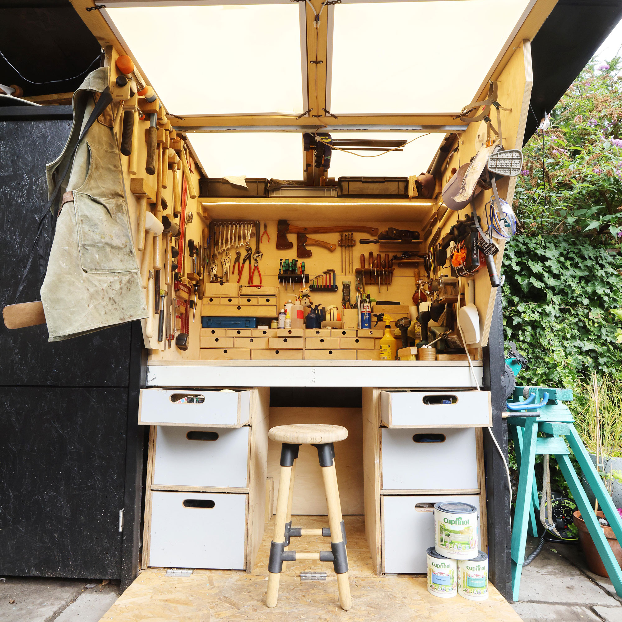 Black garden shed with wooden DIY workshop inside with a wooden stool and paint cans