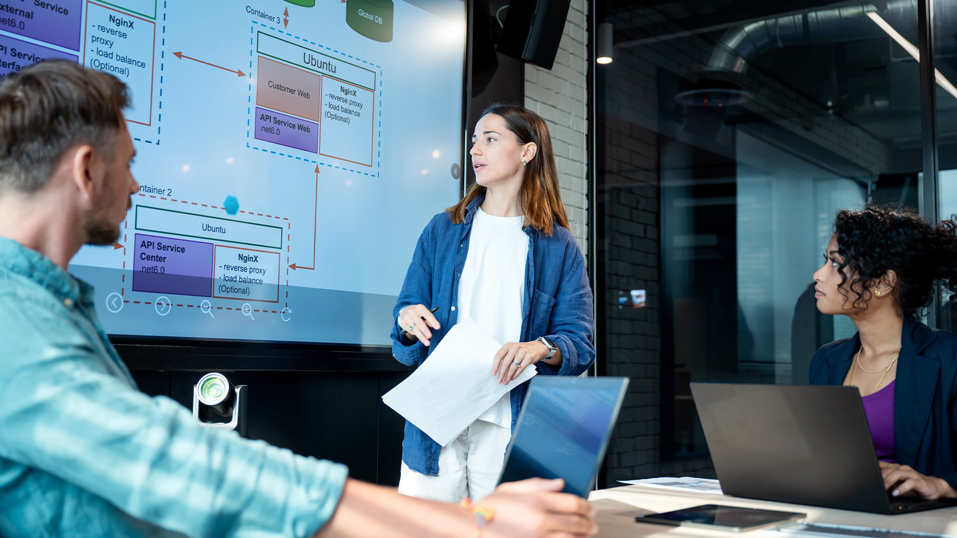 Project management concept image showing office workers in a meeting room discussing company strategy with statistics and charts on screen.