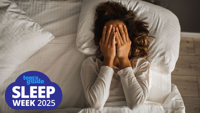 A woman lies in bed with her hands covering her face, looking upset due to sleep deprivation. A Tom&#039;s Guide Sleep Week 2025 graphic, bottom left