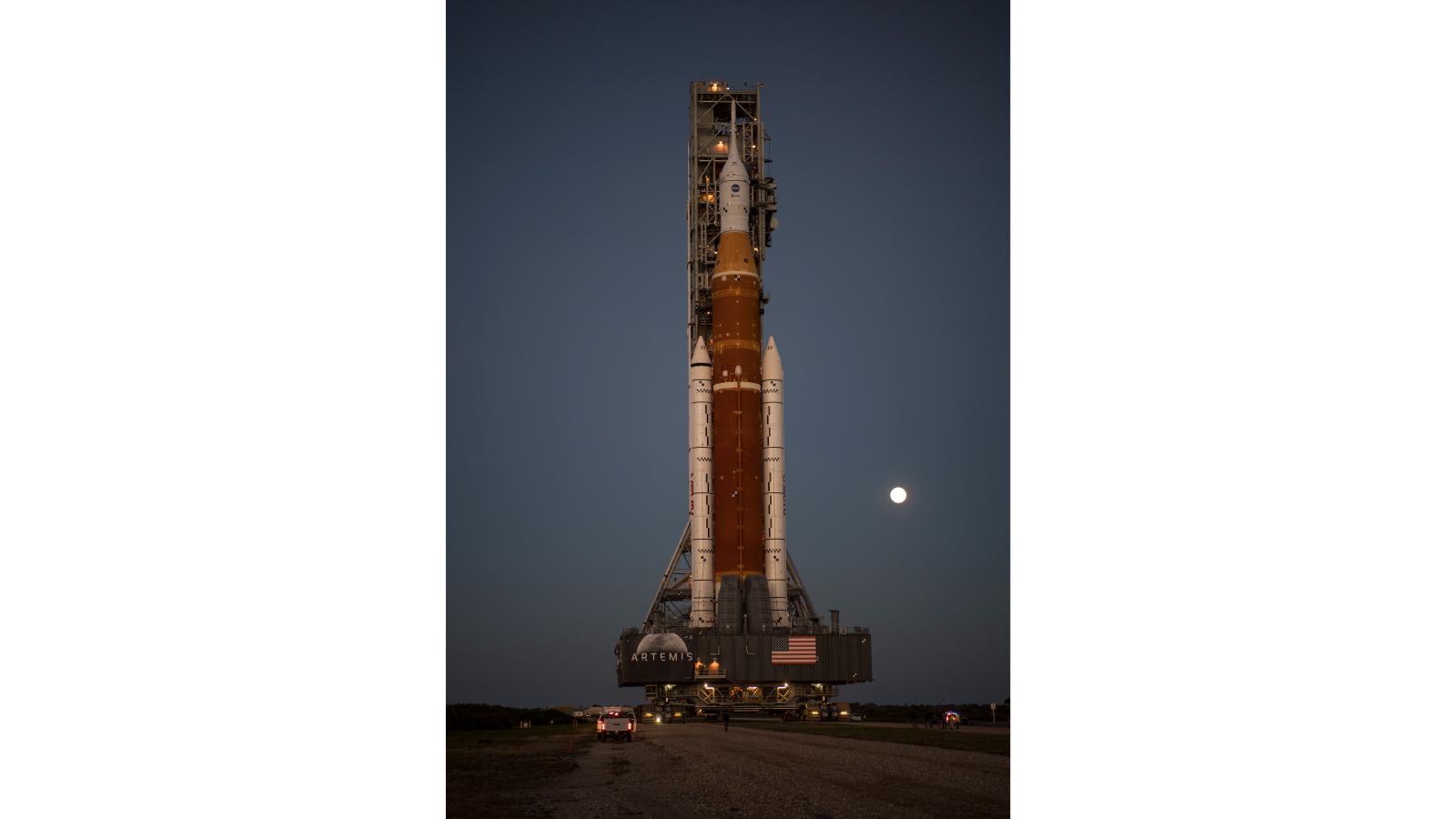 The Artemis 1 rocket is backdropped by the moon during rollout to the pad on March 17, 2022.
