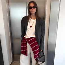 Swedish fashion creative Johanna Lager wearing chic fall 2025 outfit ideas with a gray blazer, white T-shirt, white jeans, a cord necklace with red pendant, and an ATP Atelier bag
